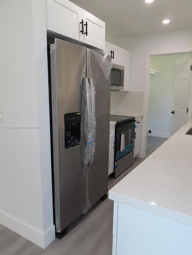 kitchen featuring light stone countertops, baseboards, light wood finished floors, appliances with stainless steel finishes, and white cabinetry