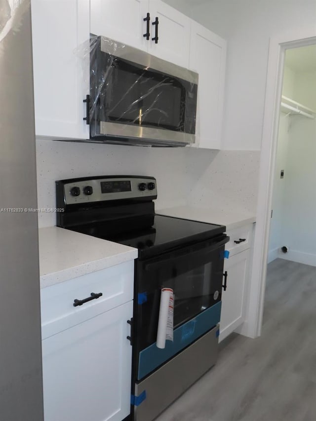 kitchen featuring light stone counters, stainless steel appliances, light wood-style floors, and white cabinets