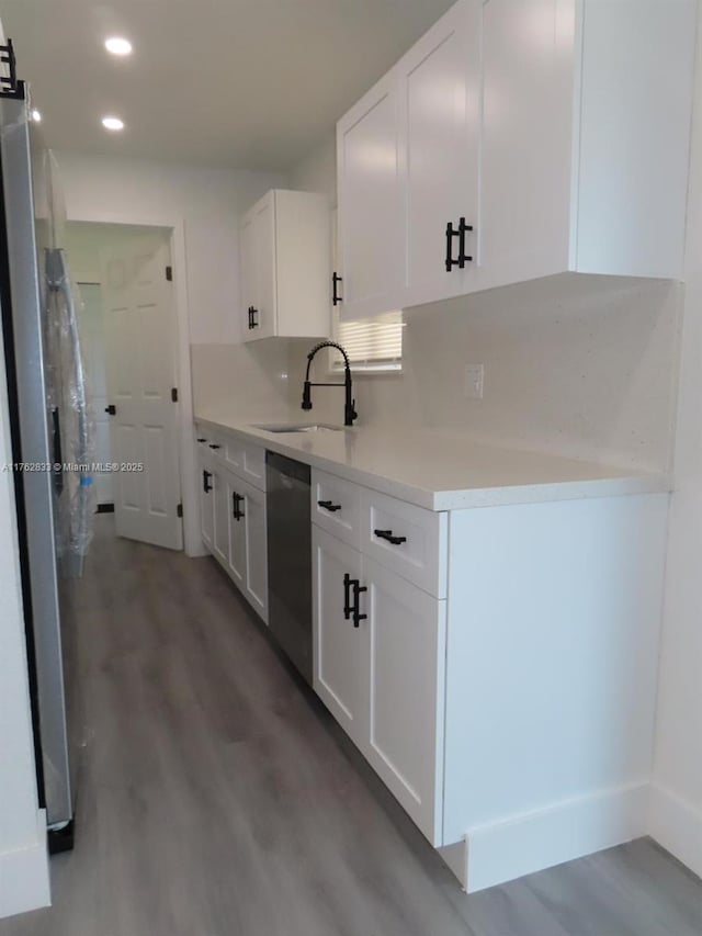 kitchen with light countertops, appliances with stainless steel finishes, wood finished floors, white cabinets, and a sink