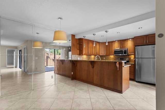 kitchen featuring brown cabinetry, dark stone counters, a peninsula, stainless steel appliances, and tasteful backsplash