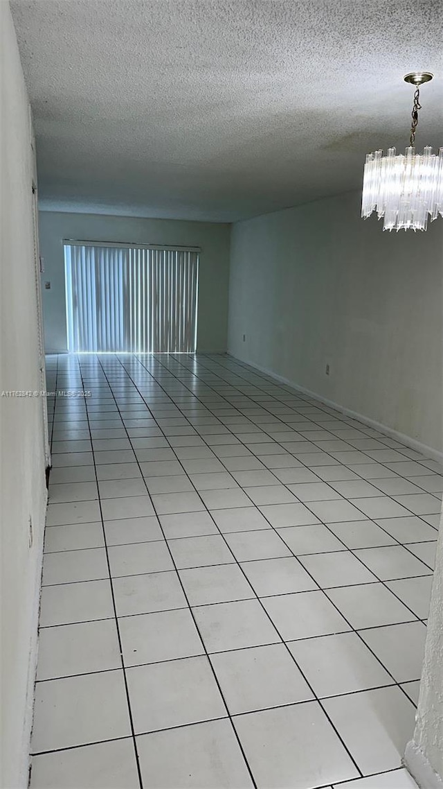 empty room featuring a textured ceiling, a chandelier, and light tile patterned flooring