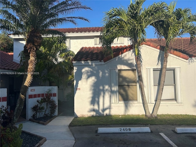 view of front of property featuring a tile roof, uncovered parking, and stucco siding