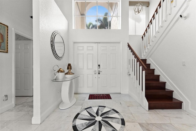 entryway with stairway, baseboards, a high ceiling, marble finish floor, and a chandelier