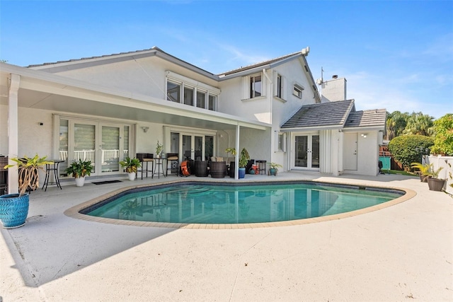 rear view of property featuring an outdoor pool, a chimney, stucco siding, french doors, and a patio area