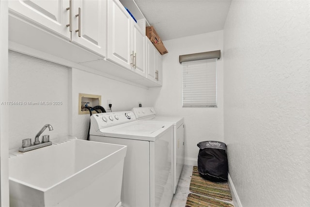 clothes washing area with independent washer and dryer, a sink, cabinet space, baseboards, and a textured wall