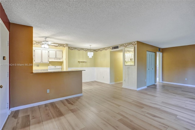 interior space featuring visible vents, light wood-type flooring, under cabinet range hood, a peninsula, and range