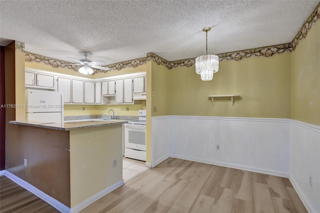 kitchen featuring under cabinet range hood, wainscoting, light wood-style floors, white appliances, and a textured ceiling