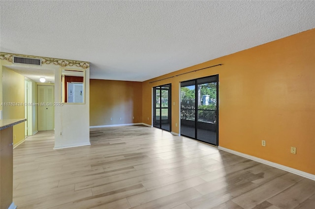 spare room featuring light wood-type flooring, visible vents, baseboards, and a textured ceiling