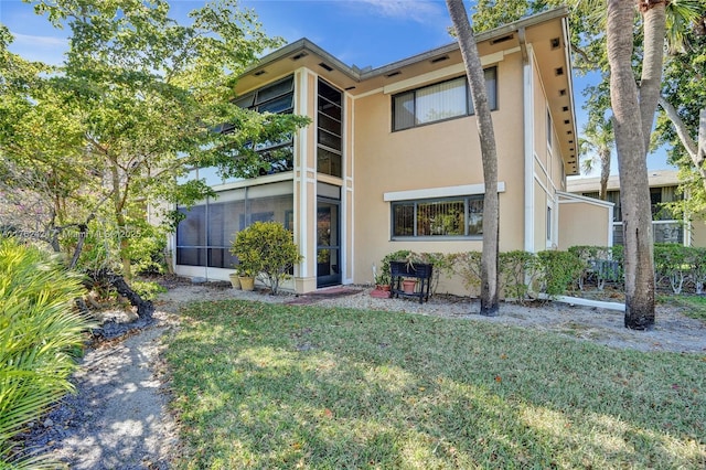 rear view of house with stucco siding, a lawn, and a sunroom