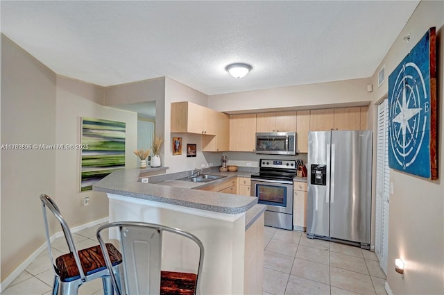 kitchen with light brown cabinets, a sink, stainless steel appliances, a peninsula, and light tile patterned flooring