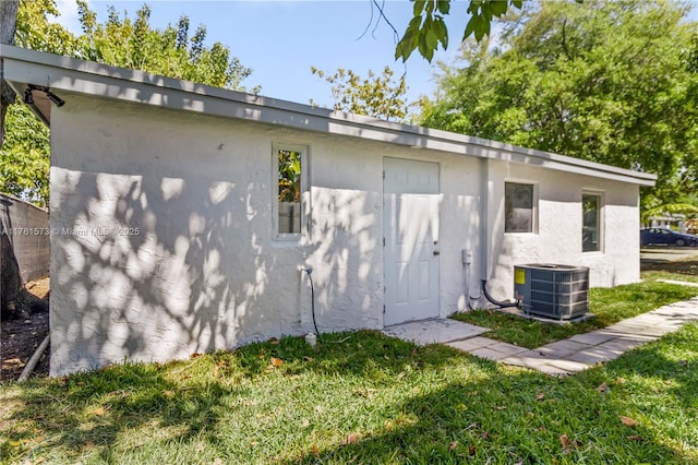back of property with central air condition unit, stucco siding, and a lawn