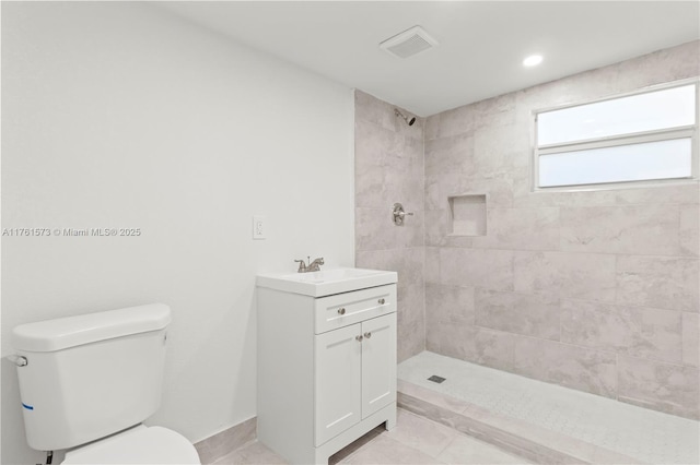 bathroom with tiled shower, vanity, visible vents, and toilet