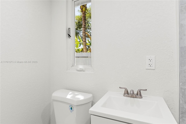 half bath featuring toilet, a textured wall, and vanity