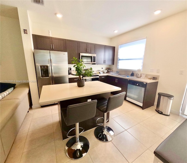 kitchen featuring a center island, stainless steel appliances, light countertops, light tile patterned floors, and dark brown cabinets