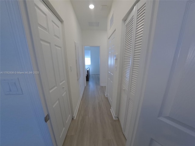 hall featuring visible vents, baseboards, and light wood-style floors