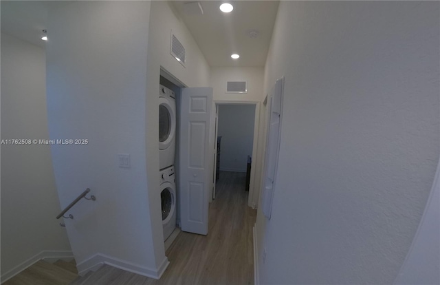 clothes washing area with stacked washer / drying machine, visible vents, light wood-style flooring, and laundry area