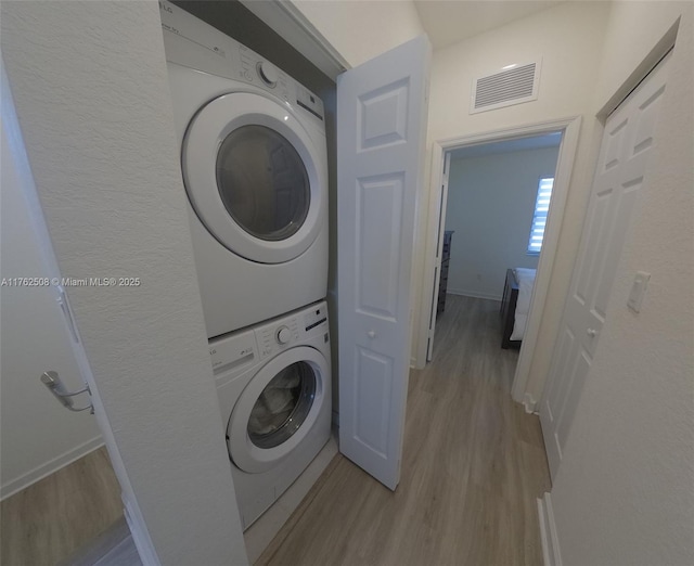 laundry room with light wood finished floors, visible vents, laundry area, and stacked washer and dryer