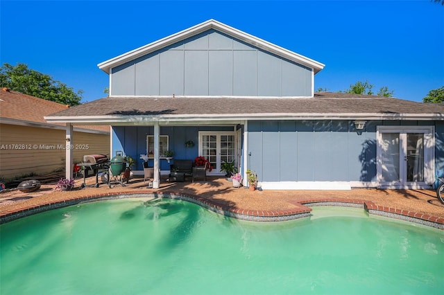 rear view of property with a patio area, an outdoor pool, french doors, and board and batten siding