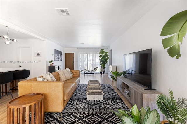 living room with visible vents, light wood-style flooring, and an inviting chandelier