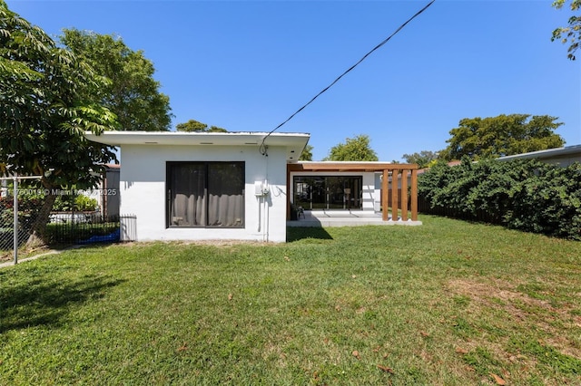 rear view of property featuring a yard, fence, and stucco siding