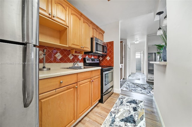 kitchen with a sink, tasteful backsplash, light wood-style floors, appliances with stainless steel finishes, and light countertops