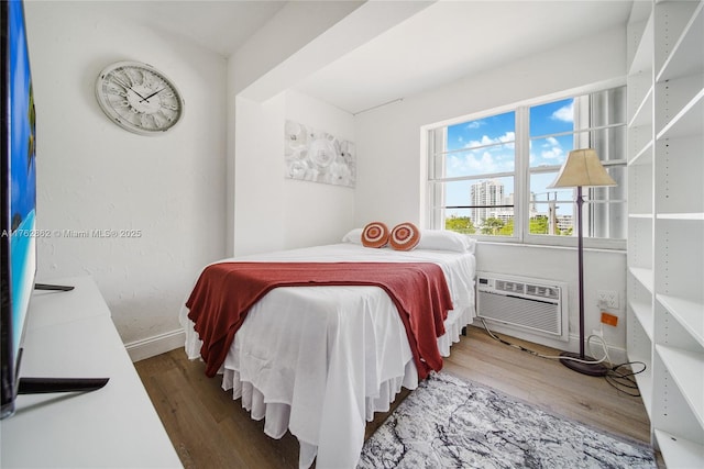 bedroom featuring an AC wall unit, baseboards, and wood finished floors