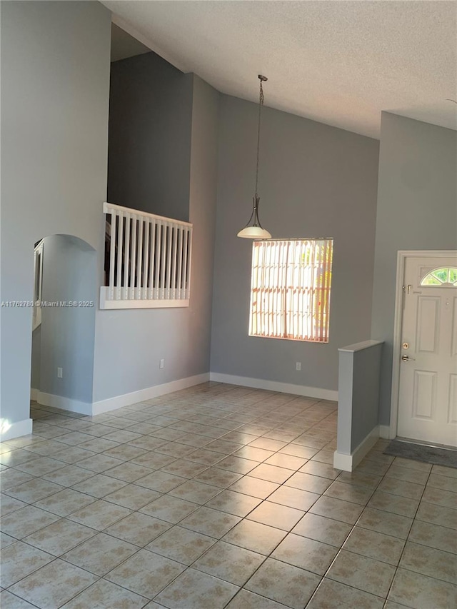 empty room featuring light tile patterned flooring, a textured ceiling, high vaulted ceiling, and baseboards