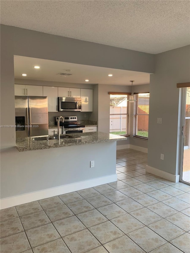 kitchen with light tile patterned floors, stone counters, a peninsula, appliances with stainless steel finishes, and white cabinetry