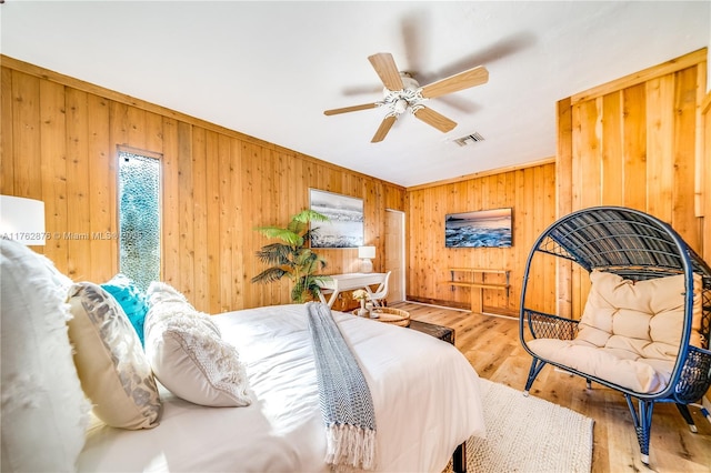 bedroom with ceiling fan, visible vents, wooden walls, and wood finished floors