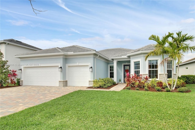 prairie-style home featuring decorative driveway, a front yard, an attached garage, and stucco siding