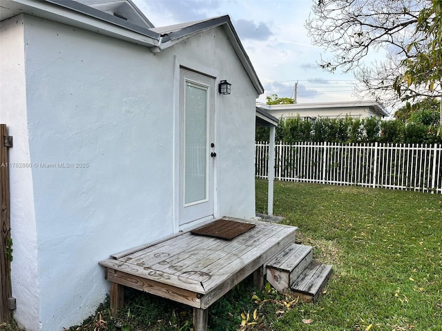 view of exterior entry with a lawn, fence, and stucco siding