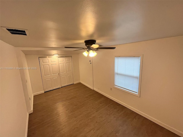 unfurnished bedroom featuring dark wood-style floors, visible vents, baseboards, ceiling fan, and a closet