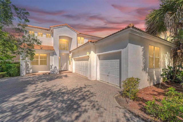 mediterranean / spanish house with stucco siding, a tiled roof, decorative driveway, and a garage