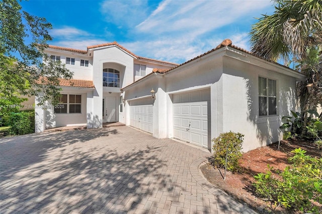 mediterranean / spanish house featuring a tiled roof, decorative driveway, an attached garage, and stucco siding