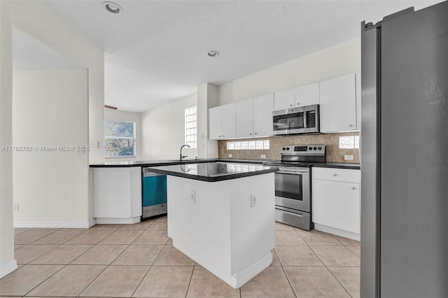 kitchen featuring a sink, dark countertops, stainless steel appliances, white cabinets, and light tile patterned floors