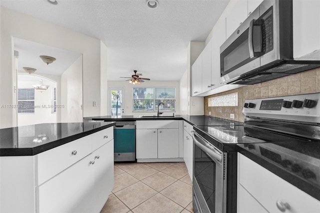 kitchen featuring dark countertops, light tile patterned floors, decorative backsplash, stainless steel appliances, and a sink