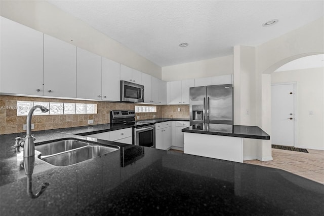 kitchen featuring a sink, dark stone countertops, appliances with stainless steel finishes, white cabinets, and decorative backsplash