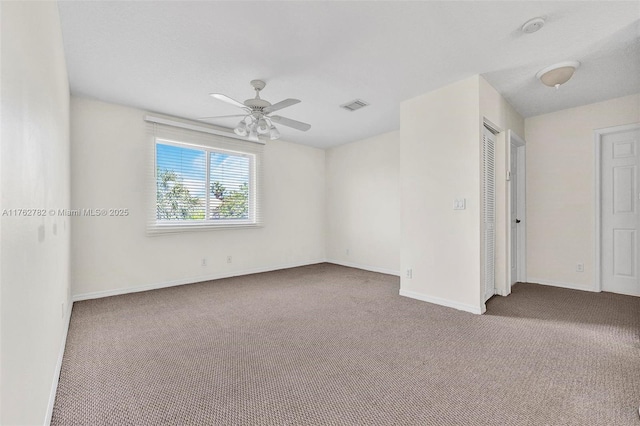 spare room with carpet flooring, ceiling fan, baseboards, and visible vents