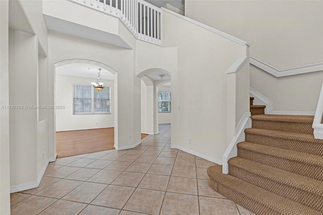 foyer featuring baseboards, stairway, light tile patterned floors, a towering ceiling, and arched walkways