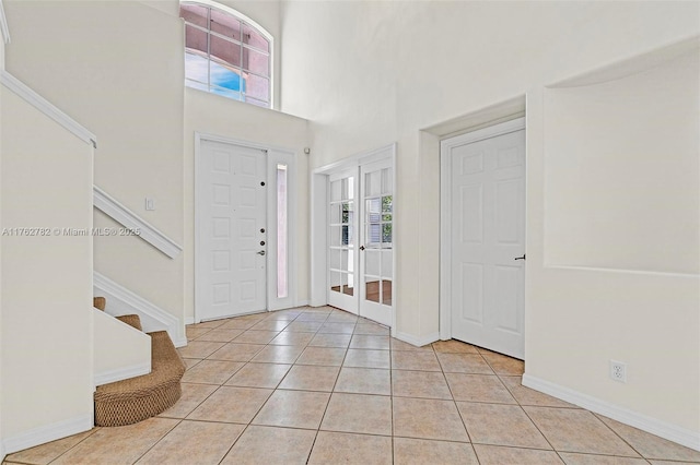 foyer with light tile patterned floors, baseboards, stairs, and a towering ceiling