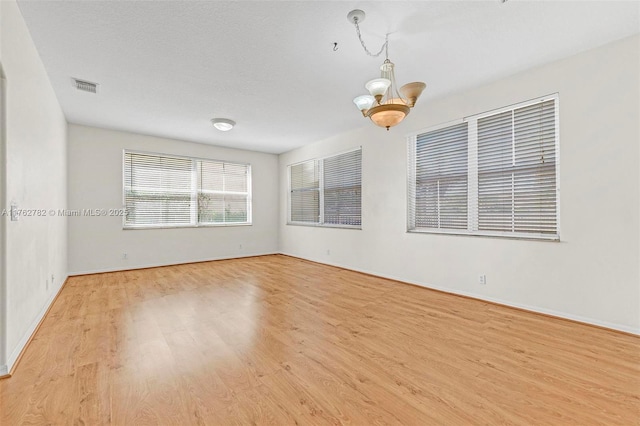 spare room with visible vents, baseboards, a notable chandelier, and light wood finished floors