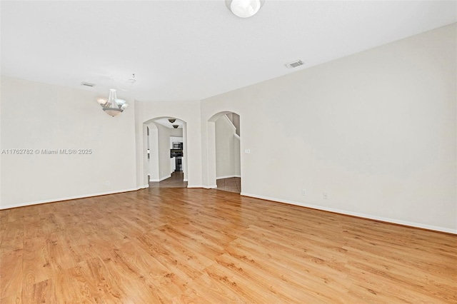 spare room featuring visible vents, baseboards, an inviting chandelier, wood finished floors, and arched walkways