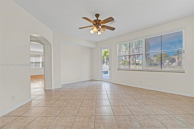 spare room with light tile patterned floors, plenty of natural light, arched walkways, and a ceiling fan