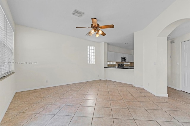 unfurnished living room featuring light tile patterned flooring, arched walkways, visible vents, and ceiling fan