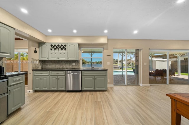 kitchen with light wood-style flooring, a sink, stainless steel dishwasher, dark countertops, and backsplash