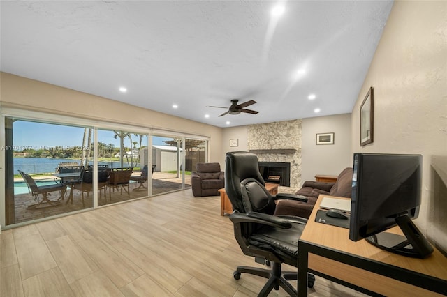 home office with recessed lighting, a fireplace, ceiling fan, light wood-style floors, and a water view