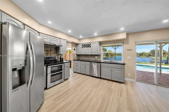 kitchen featuring gray cabinets, appliances with stainless steel finishes, under cabinet range hood, dark countertops, and tasteful backsplash