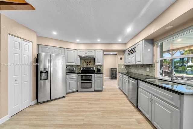 kitchen with light wood-style flooring, gray cabinets, a sink, tasteful backsplash, and stainless steel appliances