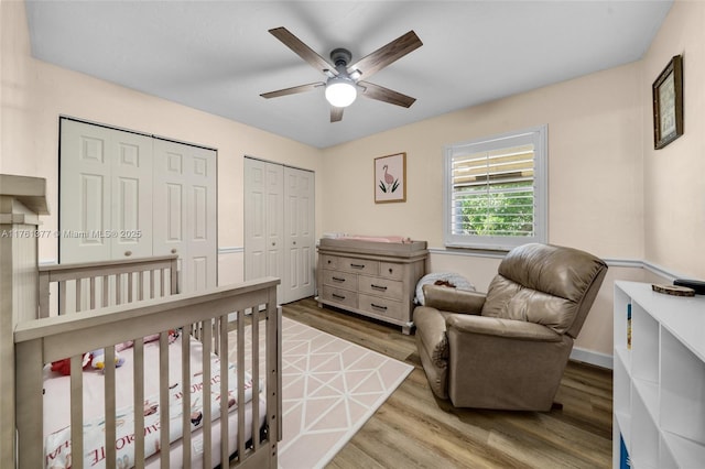 bedroom featuring baseboards, two closets, a ceiling fan, and wood finished floors