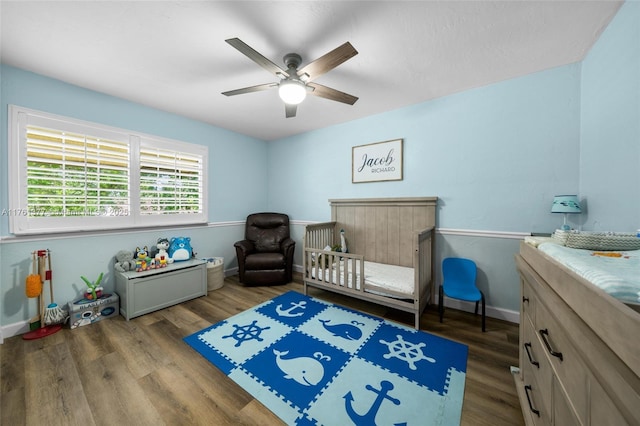 bedroom with a crib, a ceiling fan, baseboards, and wood finished floors